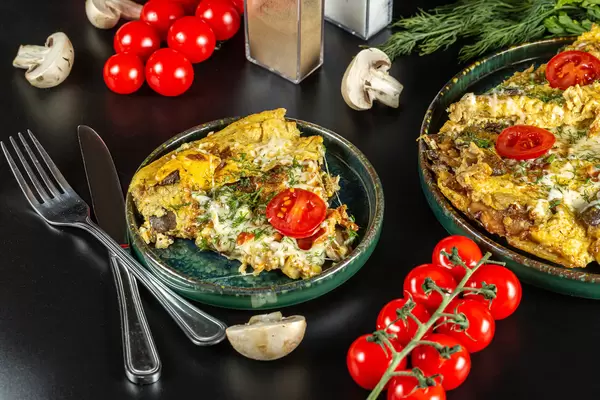 Ready egg omelet with mushrooms and mozzarella on a black background with cherry tomatoes