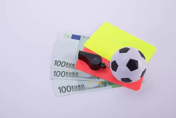 Red and yellow referee cards, a whistle and a ball with Euro banknotes