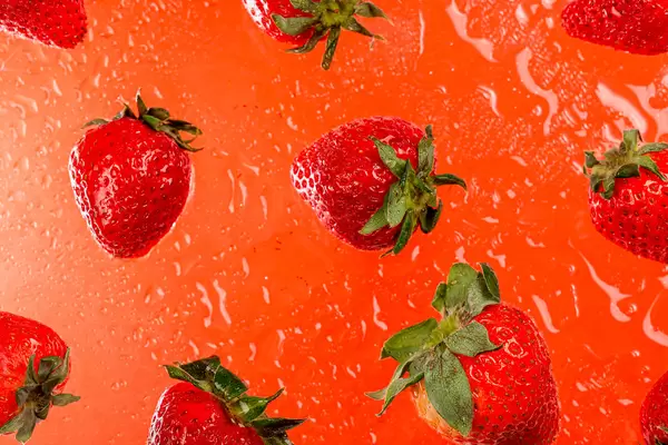 Red background with ripe strawberries and water drops