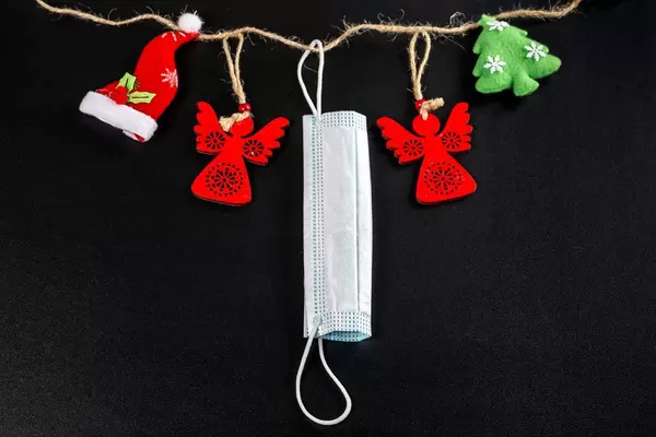 Red figurines of angels, christmas tree, red hat and medical mask hang on a rope