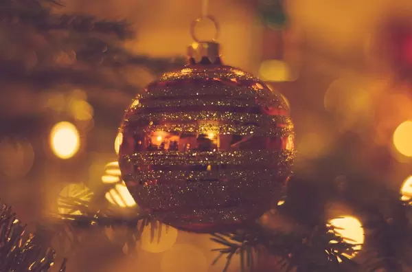 Red-golden christmas tree ball with branches and festive lights in the background