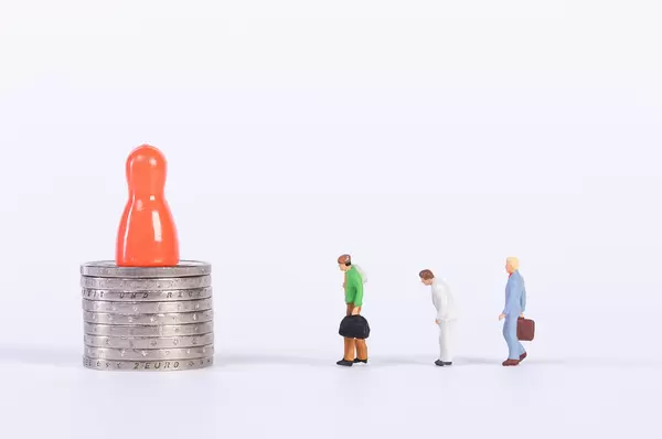 Red pawn on coin stack with miniature people on white background