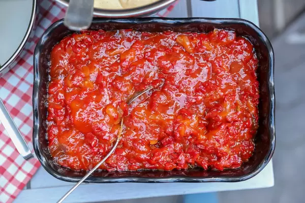 Red pepper jam dip in a black bowl with a spoon on an outdoor table