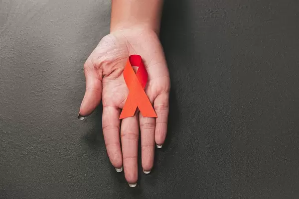 Red ribbon as symbol of aids awareness in hand on black background (Flip 2019)