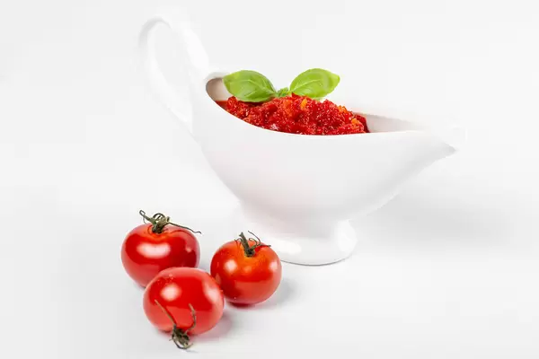 Red sauce in a white sauce bowl with basil leaves and three tomatoes