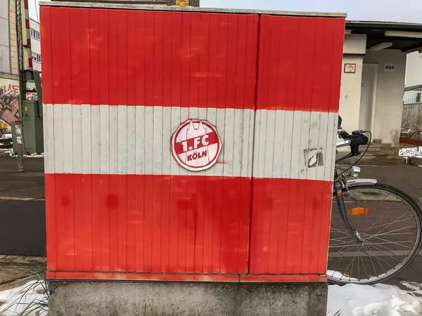 Red-white painted wall with sticker oft he football club 1. FC Köln with bicycle in the background