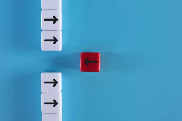 Red wooden block with arrow facing individual pointing in the different way on blue background