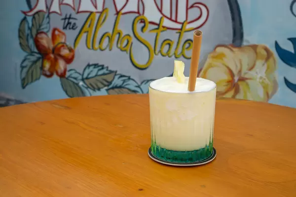 Refreshing Virgin Pina Colada in a Cocktail Glass with Bamboo Straw and Slice of Pinapple on a Wooden Table with Hawaii the Aloha State Drawing in the Background