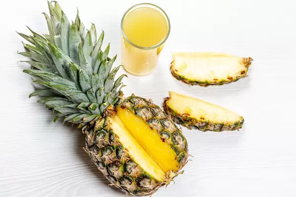 Reife Ananas aufgeschnitten neben einem Glas mit Ananassaft top-view