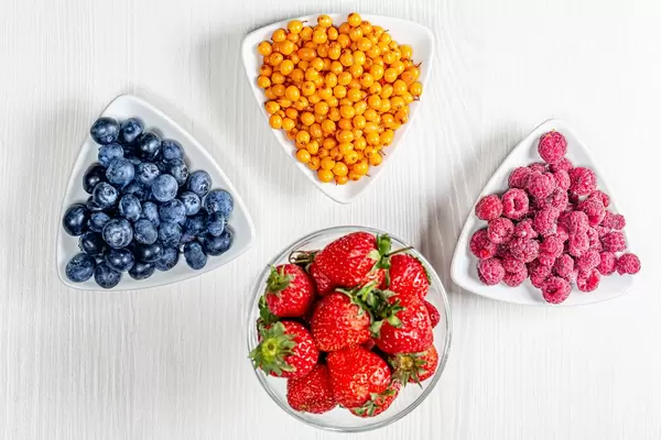 Reife Sanddornbeeren, Blaubeeren, Himbeeren und Erdbeeren auf weißem Holz-Hintergrund in top-view