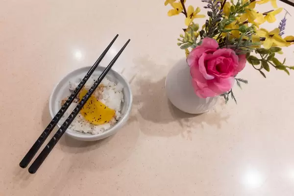 Reis in der Schüssel, Essstäbchen und Blumen in der Vase