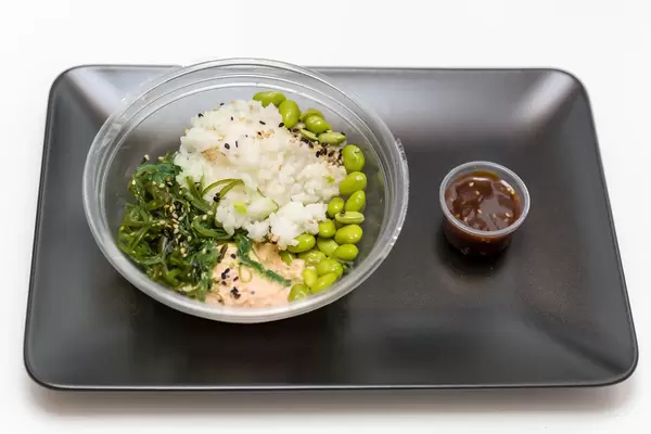 Reis mit Seealgensalat, Sojabohnen und Lachscreme in Plastikschale und Soße auf Teller