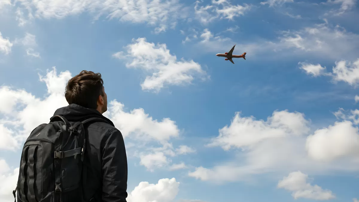 Reisender mit Rucksack beobachtet Flugzeug am Himmel