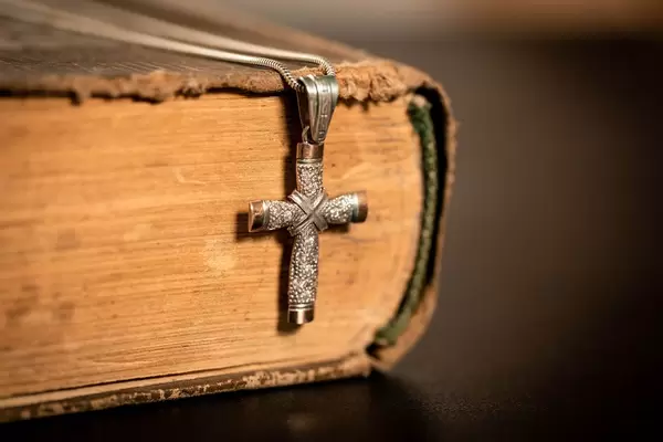 Religiöses Buch mit abgenutztem Einband und darübergelegter Halskette mit Kreuzanhänger