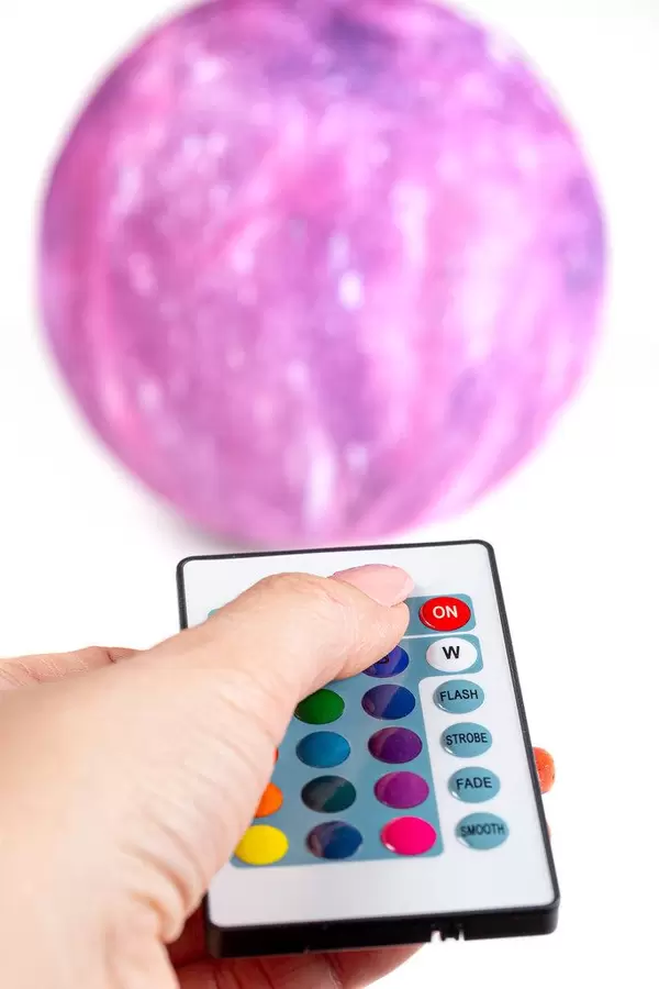 Remote control in a woman's hand, in the background nightlight-planet