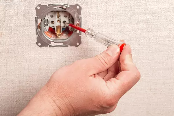 Renovation and electricity and people concept - close up of electrician hands with screwdriver checking for current availability