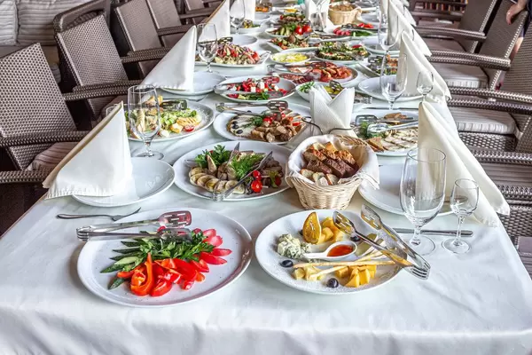 Restaurant table covered with a tablecloth with Cutlery, glasses and different types of food and snacks (Flip 2019)