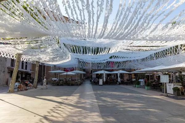 Restaurants mit Tischen draußen und weiße Straßendeko auf Plaça Major in Pollença, Mallorca