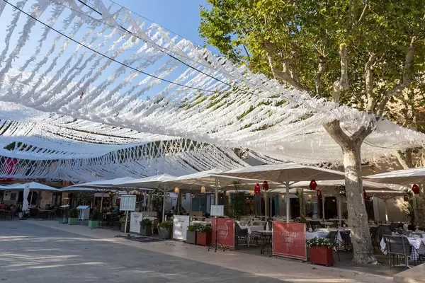 Restaurants with outdoor tables and white street decoration in Plaça Major, main square of Pollença