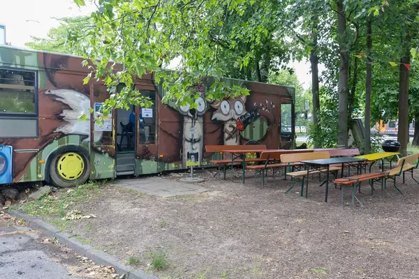 Retro-Bus voll von bunten Graffities mit Biertische im Vordergrund im BaseCamp Hostel in Bonn