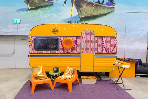 Retro-Wohnwagen mit lila Teppich, zwei orangen Sessel und einem Synthesizer im Vordergrund