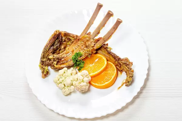 Ribs of young lamb with fresh orange and cauliflower on a white plate (Flip 2019)