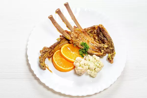 Ribs of young lamb with fresh orange and cauliflower on a white plate