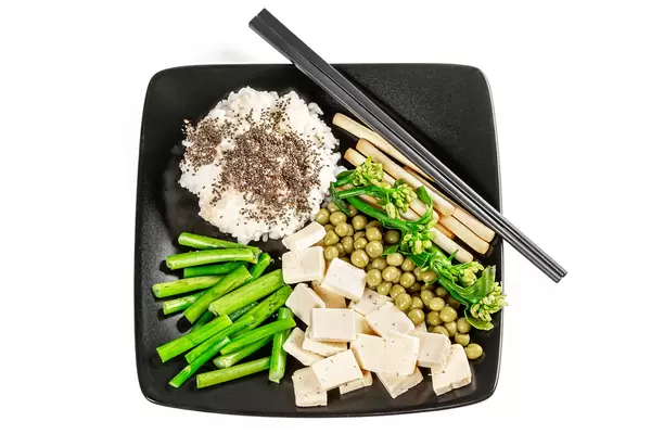 Rice, peas, broccolini, cheese and chia seeds on a black plate, top view
