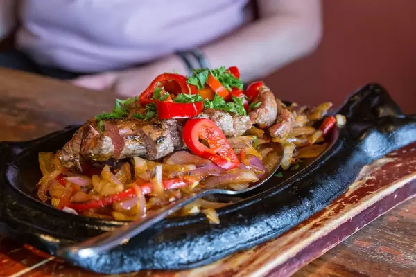 Rindfleisch-Fajitas mit gegrilltem Rinderfilet, in Scheiben geschnitten, Gemüse, Kräutern und Zwiebeln, auf einem schwarzen Steinteller