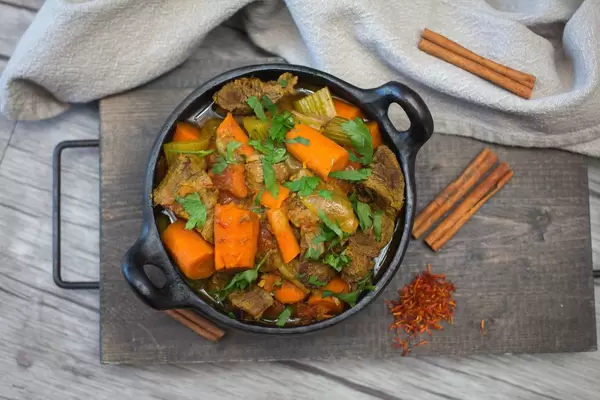 Rindfleisch-Tajine mit Karotten, Sellerie und Petersilie mit Zimtstangen und Safran auf Holzbrett