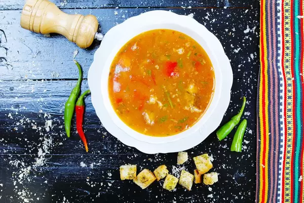 Rindfleischsuppe mit Croutons, Pfeffer und Chilis, Flatlay auf schwarzem Hintergrund