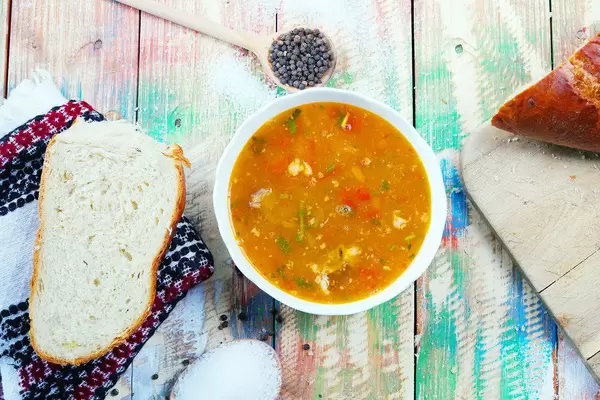 Rindfleischsuppe serviert mit Weißbrot, Salz und Pfeffer. Bunter Holztisch im Vintage-Stil