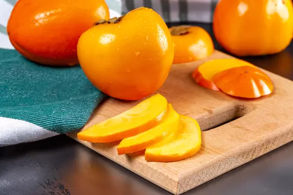 Ripe, juicy persimmons whole and chopped on a kitchen board