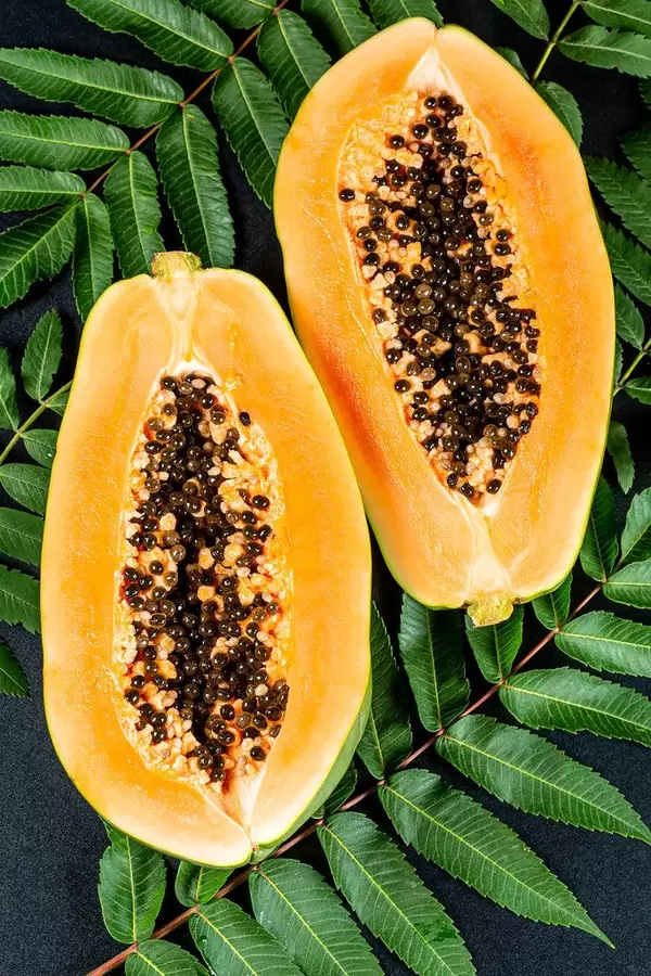 Ripe papaya halveson a black background with leaves, top view