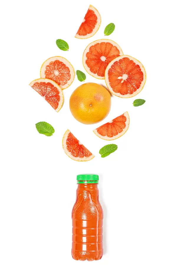 Ripe whole grapefruit and slices with mint leaves on white with a bottle of juice, top view