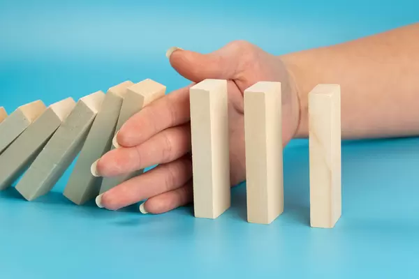Risk and strategy in business, close up of hand stopping wooden block from falling in the line of domino
