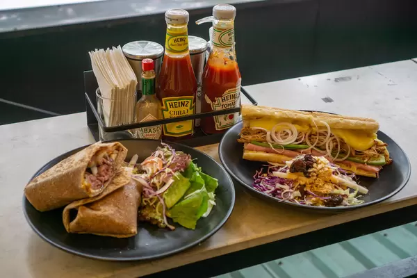 Roast Beef Tortilla Wrap with Green Salad and Pulled Pork Sandwich with Coleslaw on a Restaurant Table with Sauces, Salt and Pepper
