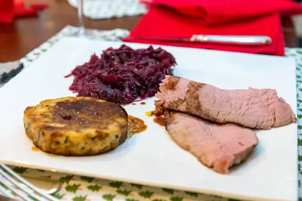 Roastbeef mit flachem Knödel und Rotkraut auf weißem Teller