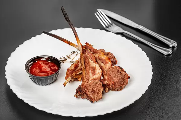 Roasted lamb ribs with sauce on plate, black background