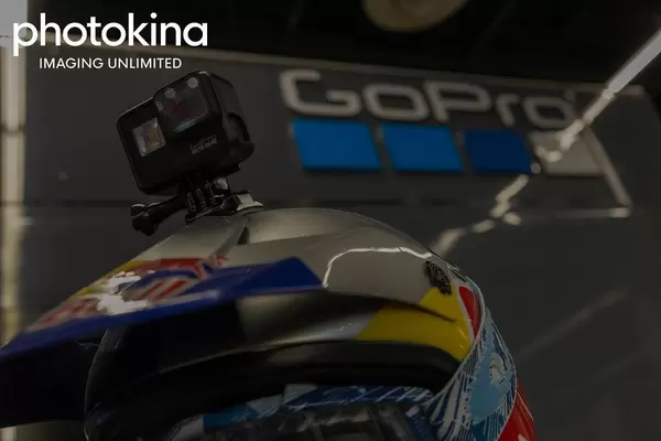 Robuste Actionkamera von GoPro mit Helmhalterung auf einem RedBull-Rennfahrerhelm, neben dem Bildtitel "photokina imaging umlimited"