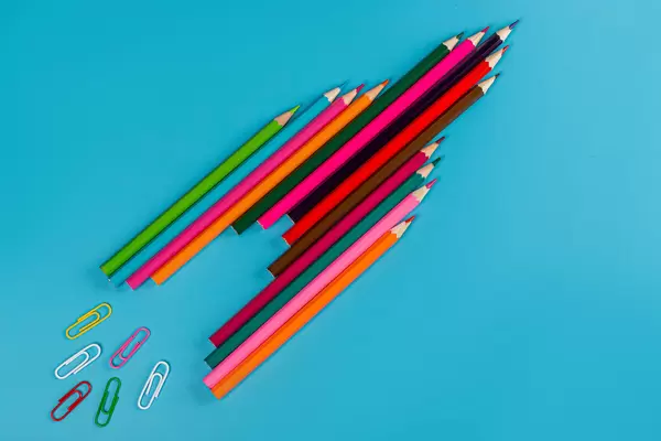 Rocket made of colored pencils and paper clips on blue background