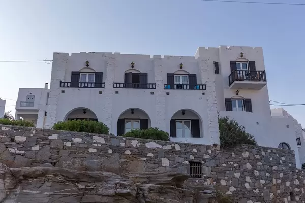Rocks and wall in front of a Greek house with Mediterranean balconies, made of white limestone, on the Aegean island Paros
