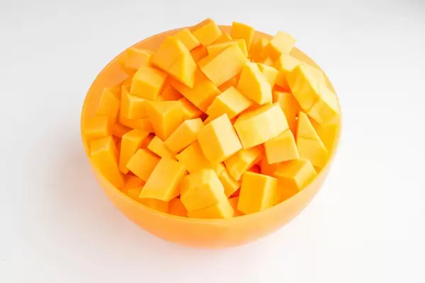 Rohe Kürbisstücke in einer orangenfarbigen Schüssel auf weißem Hintergrund