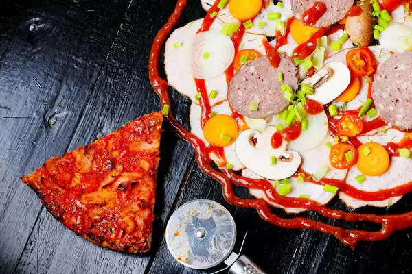 Rohe Pizzazutaten neben einem gebackenen Pizzastück und einem Pizzaschneider