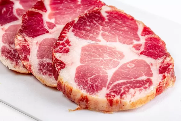 Rohe Schweinekotelett Scheiben auf einem weißem Schneidebrett Nahaufnahme