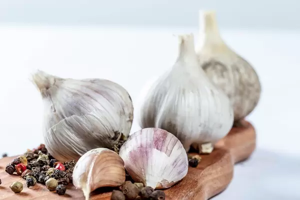 Roher Knoblauch und getrocknete Pfefferkörner auf Holzbrett vor weißem Hintergrund