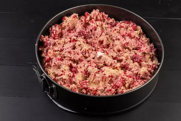 Roher, roter Kuchenteig mit Erdbeeren in einer Backform auf einem schwarzen Holztisch
