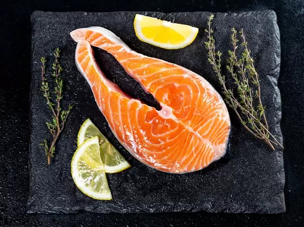Rohes Lachsfilet mit Zitronenscheiben und Kräutern auf schwarzer Schieferplatte