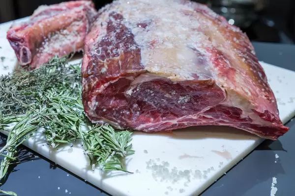 Rohes, tiefgefrorenes Fleisch mit Kräutern auf einem Küchenbrettchen