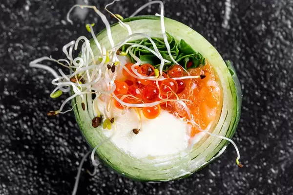 Roll with cucumber, salmon, cheese, arugula, micro greenery and red caviar on a black background. Top view